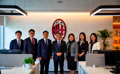 米兰中国官方运营中心团队在现代化办公室内的合影，背景有俱乐部徽章